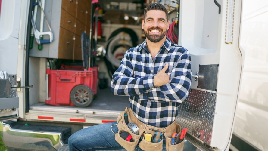 Smiling man with a tool belt standing in front of his tool trailer
